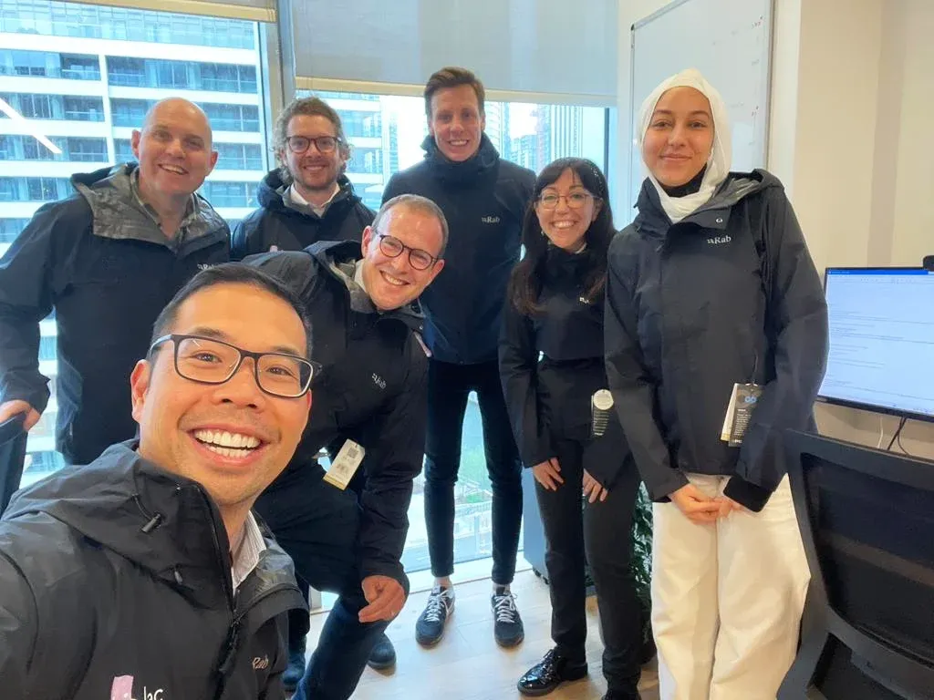 Six team members in matching black jackets posing together in an office