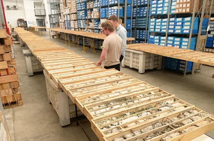 Two people beside long tables of core trays in a core-storage warehouse